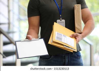 Young courier with parcels and clipboard indoors, closeup. Delivery service
