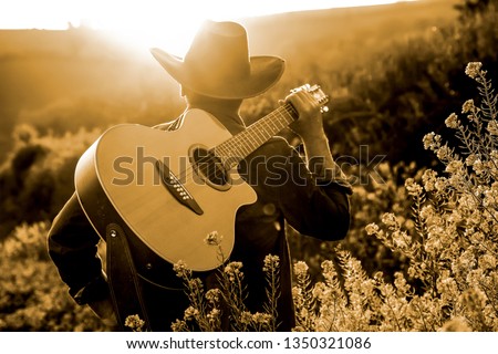 a young cowboy with his guitar at the countryside of Texas on a sunset evening