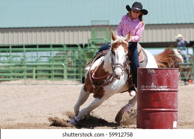 Young Cowgirl Riding A Beautiful Paint Horse In A Barrel Racing Event At A Rodeo.