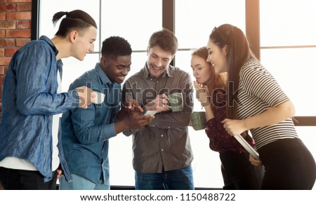 Young coworkers smiling, while looking at funny photo or watching video on mobile phone during coffee break, copy space