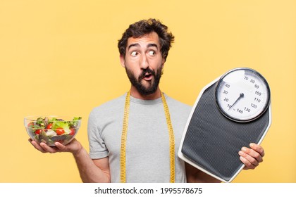 young crazy bearded man dieting doubting or uncertain expression and holding a scale and a salad