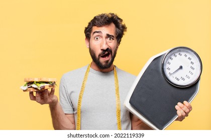 young crazy bearded man dieting doubting or uncertain expression and holding a weight scale and a sandwich