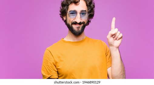 young crazy cool man smiling cheerfully and happily, pointing upwards with one hand to copy space against flat wall - Shutterstock ID 1946890129
