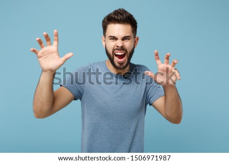 Young crazy man in casual clothes posing isolated on blue background in studio. People sincere emotions lifestyle concept. Mock up copy space. Shouting, growling like animal, making cat claws gesture
