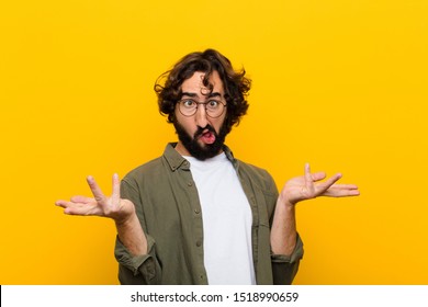 young crazy man shrugging with a dumb, crazy, confused, puzzled expression, feeling annoyed and clueless against yellow wall