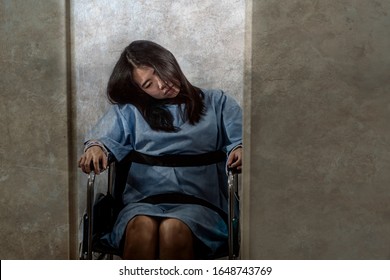 young crazy and mentally insane Asian woman restrained in wheelchair at mental hospital suffering psychiatric disorder as schizophrenia looking catatonic in Korean horror movie style