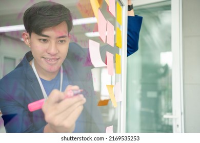 Young Creative Businessman Holding A Marker And Writing Plan And Share Idea On Glass Wall With Sticky Note, Brainstorming And Discussing And Formulating, Business Strategies In Tech Startup Office.