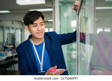 Young Creative Businessman Holding A Marker And Writing Plan And Share Idea On Glass Wall With Sticky Note, Brainstorming And Discussing And Formulating, Business Strategies In Tech Startup Office.