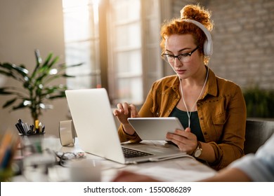 Young creative businesswoman working on digital tablet while wearing headphones in the office.  - Shutterstock ID 1550086289