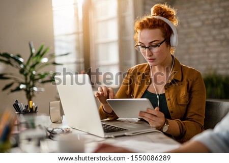 Young creative businesswoman working on digital tablet while wearing headphones in the office. 