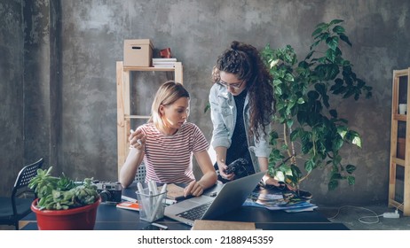 Young creative colleagues are planning design, drawing layout in notebook and watching photos on camera screen. Women are busy working on important project. Desk with office supplies in foreground. - Powered by Shutterstock