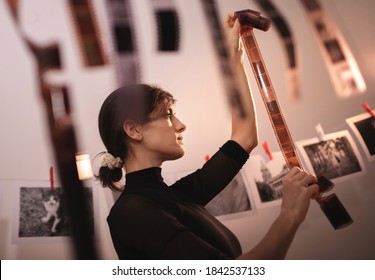 Young creative female holding filmstrip. Portrait of creative girl photographer in photo studio darkroom. Developing analog camera film - Powered by Shutterstock