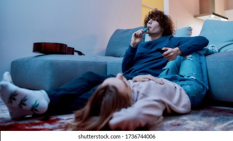 Young creative guy smoking marijuana from a vape pen or vaporizer while relaxing with his girlfriend in the living room. Cannabis vaporizer. E-cigarette. Weed legalization. Ganja, friends smoking