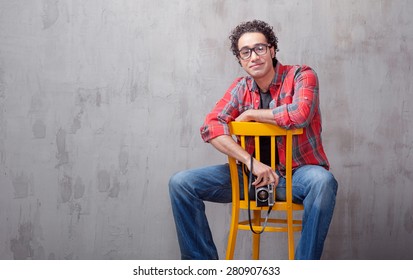 Young and creative. Handsome young Afro-American man holding camera and smiling while sitting on a chair against grey background - Powered by Shutterstock