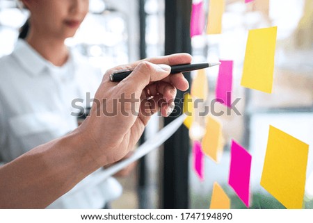 Young creative team professional using post it notes in glass wall to writing strategy business plan to development grow to success.