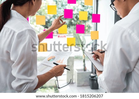Young creative team professional using post it notes in glass wall to writing strategy business plan to development grow to success.