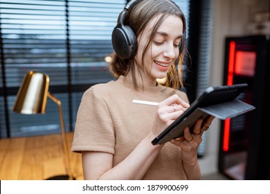 Young creative woman enjoying music in headphones, mixing music on a digital tablet in home studio