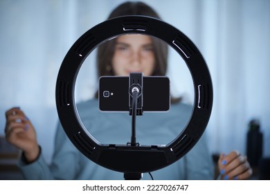 Young creative woman live streaming a video for her followers on social media, she is using her smartphone and a ring light