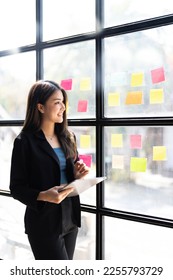 Young creative woman professional using sticky notes in glass wall to writing strategy business plan to development grow to success. Happy asian woman working at office. - Shutterstock ID 2255793729