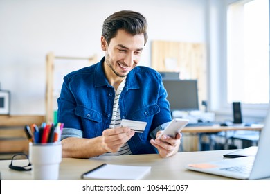 Young creative worker using credit card and phone to order lunch while working in office
