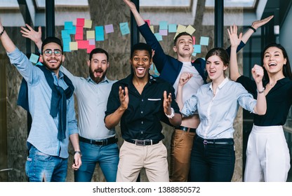 Young crew of happy excited male and female business partners celebrating completed startup project while looking at camera and laughing, overjoyed colleagues feeling amazed of done good work