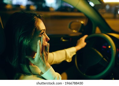 Young Crying Woman Driving Car At Night And Wipes Away Her Tears. 