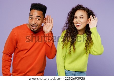 Young curious ouple two friends family man woman of African American ethnicity wear casual clothes together try to hear you overhear listening intently isolated on pastel plain light purple background