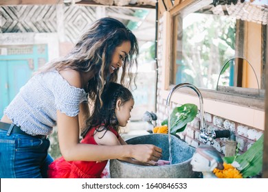 Young Curly Asian Woman With Little Cute Girl Washing Hands In Sink Together Standing On Outside Terrace In Ethnic Style