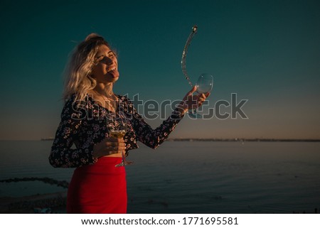young curly blonde fooling around with glasses in hand on a background of sky and sea