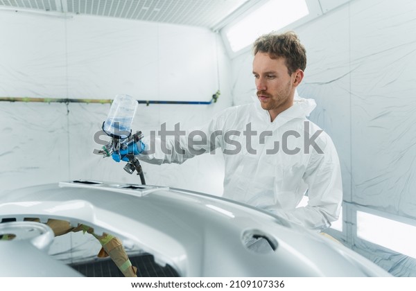 Young curly car\
painter varnishes a car bumper. Man works in a spray booth. Process\
of painting car body\
parts