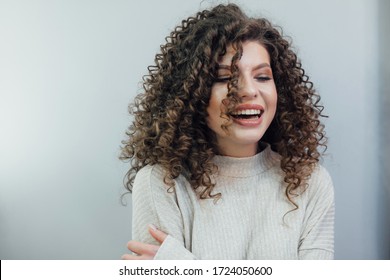 Young curly girl smiling in a white sweater