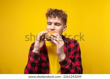 young curly guy student eats a burger on a yellow background, a man with fast food