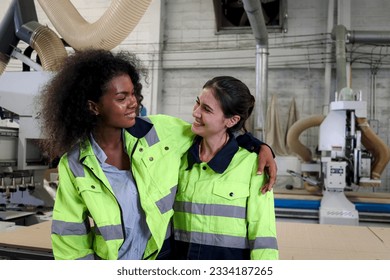 Young curly hair woman worker in safety vest hugging her friend co-worker in factory, two beautiful industrial female mechanic technician engineers working together in construction area workplace. - Powered by Shutterstock