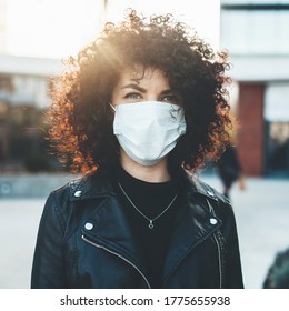 Young Curly Haired Woman Wearing A Medical Mask Outside Posing At Camera In A Sunny Day