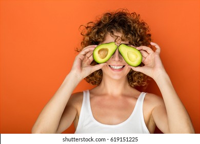 young curly woman holding a avocado in hands on orange background