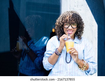 Young Curly Woman With Juice Cup Standing Over Dark Background And Light Reflection. Portrait Of A Smiling Woman With Curly Hair.