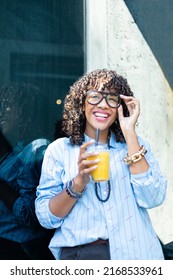 Young Curly Woman With Juice Cup Standing Over Dark Background And Light Reflection. Portrait Of A Smiling Woman With Curly Hair.