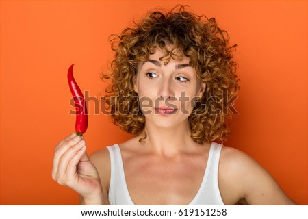 young curly woman on orange background with chili pepper