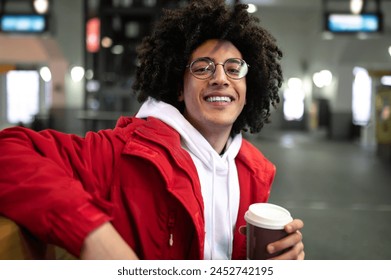 Young curly-haired guy having coffee and waiting for the train at the railway station - Powered by Shutterstock