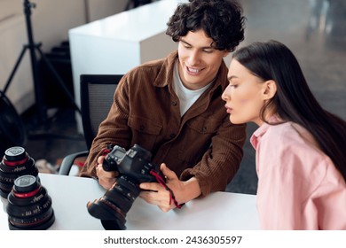 Young, curly-haired male photographer shows the camera screen to an attentive female model in pink shirt, collaborating during studio photo shoot - Powered by Shutterstock