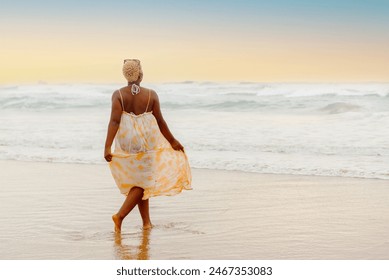 young curvy black girl in summer dress strolls along the shore of the beach walking towards the sea at sunset - Powered by Shutterstock