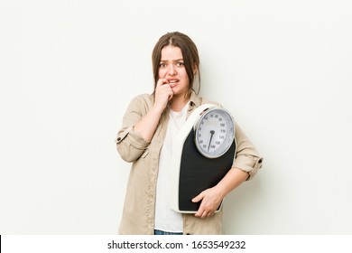 Young curvy woman holding a scale biting fingernails, nervous and very anxious.