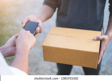 Young Customer Man Signing On  Smartphone To Take Box From Professional Delivery Man At Home