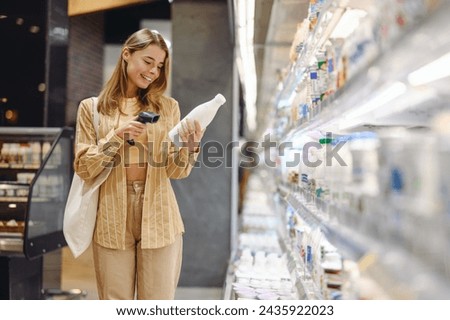 Young customer woman in casual clothes hold check scan barcode of bottle of milk shopping at supermaket store in dairy department buy choose product in hypermarket. Purchasing food gastronomy concept