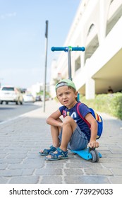 Young Cute Boy Is Sitting On The Kick Scooter At A Bus Stop Near The Emirates Mall In Dubai, Waiting For The Bus. United Arab Emirates, Road To The Beach, Traffic.