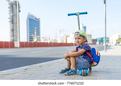 Young Cute Boy Is Sitting On The Kick Scooter At A Bus Stop Near The Emirates Mall In Dubai, Waiting For The Bus. United Arab Emirates, Road To The Beach, Traffic.