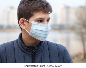 Young Cute Caucasian Boy Wearing Protective Mask Against The Corona Virus On The Street. Teenager In Surgical  Face Mask To Prevent From Virus Covid 19 In The City.  Close Up Portrait