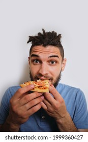 Young Cute Caucasian Man With Beard And Dreadlocks Eats Pizza On White Neutral Background. Human Holds Piece Of Cheese Pizza With Tomatoes In His Hands And Enjoys Eating. Vertical Image.