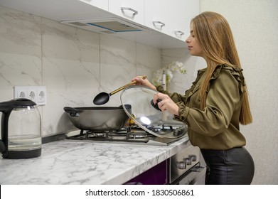 Young Cute Caucasian Woman In Black Leather Tights Cooking At Purple And White Modern Kitchen Designed In Minimalist Style