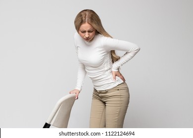 Young cute Caucasian woman having pain, muscle or chronic nerve pain in her back, hold the chair/Health Issue, diseases of musculoskeletal system concept/Diseases of spine, scoliosis, osteoporosis